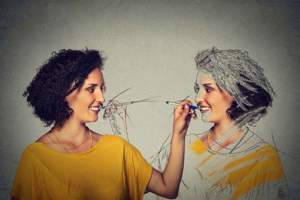 Two women face each other, one real and the other as a drawing, as if creating one another with pencils.