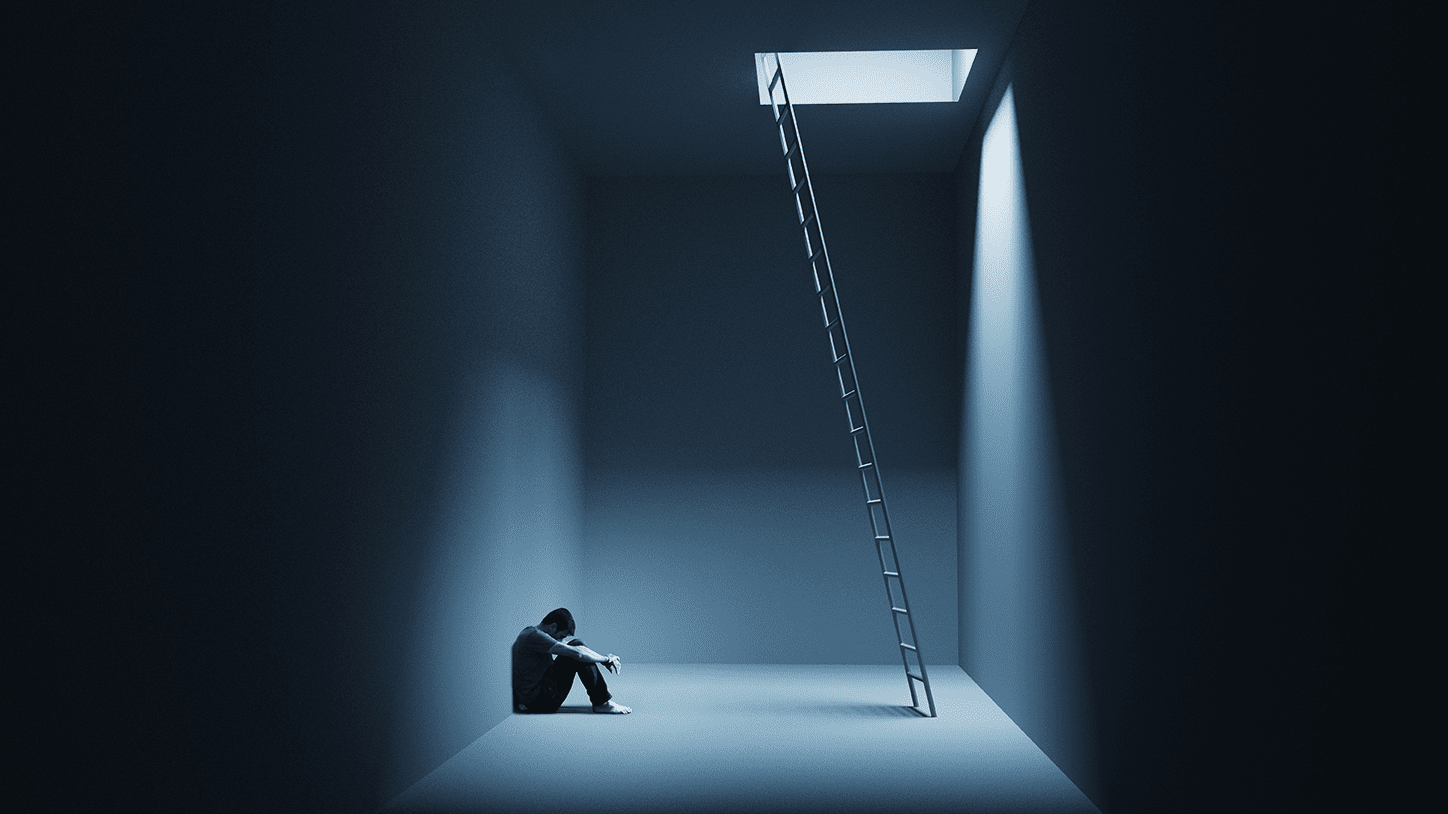 A person sits despondently in a dark room with a ladder leading to a bright opening above.